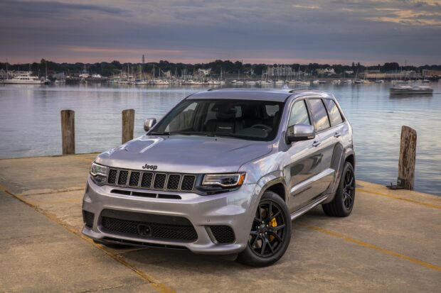 A silver Jeep Grand Cherokee is parked on a concrete dock near a calm marina with boats in the background, 2K Desktop Wallpaper