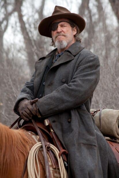 A man wearing a hat and eyepatch riding a horse in a winter forest scene with Jeffrey Bridges, 2K Mobile Wallpaper