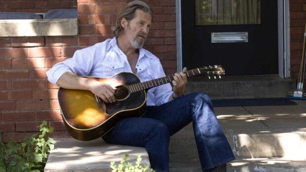 Jeffrey Bridges plays guitar on a porch with a brick wall background, HD Desktop Wallpaper