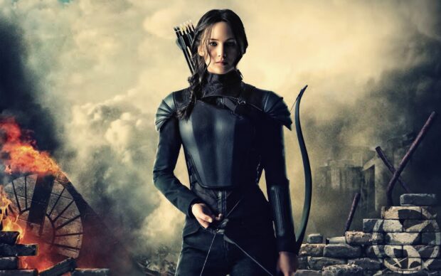 Jennifer Lawrence in a battle ready stance holding a bow amid destruction from The Hunger Games, HD Desktop Wallpaper