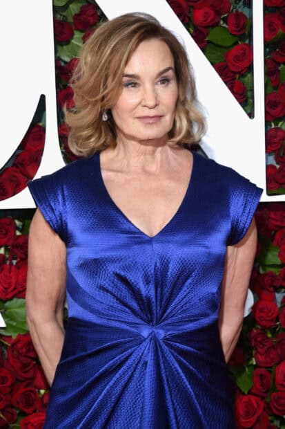 Jessica Lange in a blue dress standing in front of red roses with elegant earrings, 2K Mobile Wallpaper