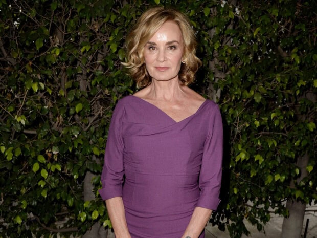 Jessica Lange stands in front of green foliage wearing a purple dress, HD Desktop Wallpaper