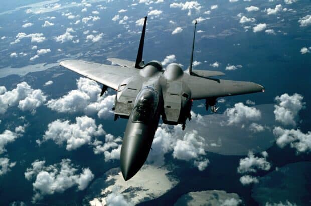 A jet fighter flies high above clouds and water in the sky, 2K Desktop Wallpaper