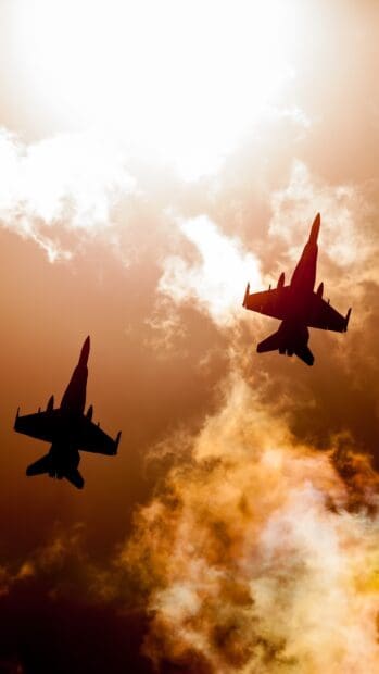 Two jet fighters fly through a fiery orange sky with dramatic clouds during sunset, 2K Mobile Wallpaper