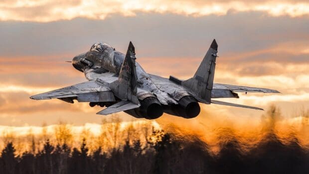 A jet fighter flies low as the sun sets behind a forested horizon, HD Desktop Wallpaper
