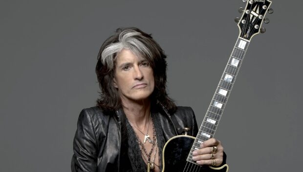 Joe Perry holding a black guitar with a serious expression in a studio setting, 2K Desktop Wallpaper