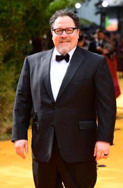 Jon Favreau is wearing a black tuxedo and glasses while smiling on a yellow carpet, 2K Mobile Wallpaper