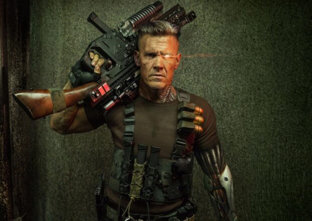 Josh Brolin stands with a high tech weapon and robotic arm in a dark setting, HD Desktop Wallpaper