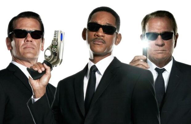 Josh Brolin stands with two men wearing black suits and sunglasses holding futuristic weapons, HD Desktop Wallpaper