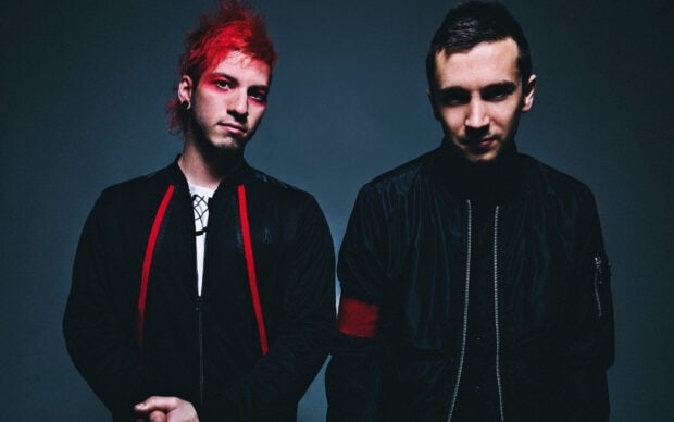Josh Dun stands with red hair and face paint in a dark setting, 2K Desktop Wallpaper