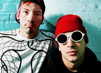 Josh Dun and a bandmate posing in front of a turquoise wall with distinctive clothing and accessories, HD Desktop Wallpaper