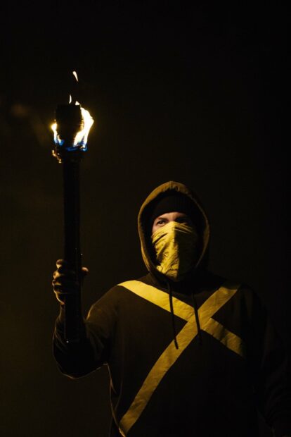 A person wearing a yellow mask and hoodie holds a lit torch in the dark with a serious expression, HD Mobile Wallpaper