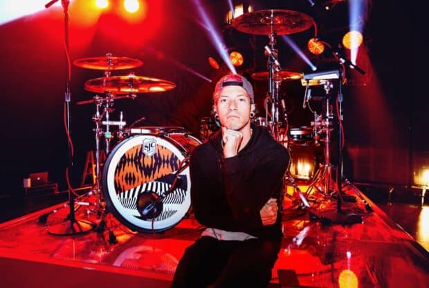 Josh Dun is sitting thoughtfully by his drum set on stage with red lighting, HD Desktop Wallpaper