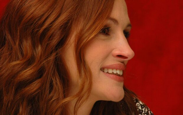 Julia Roberts is smiling with her side profile visible against a red background, HD Desktop Wallpaper
