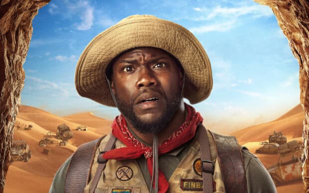 A man wearing a hat and red scarf stands in a desert with old vehicles in the background, 2K Desktop Wallpaper
