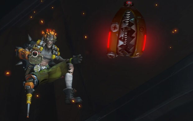 Junkrat is shown setting a fiery trap in a dark environment, HD Desktop Wallpaper