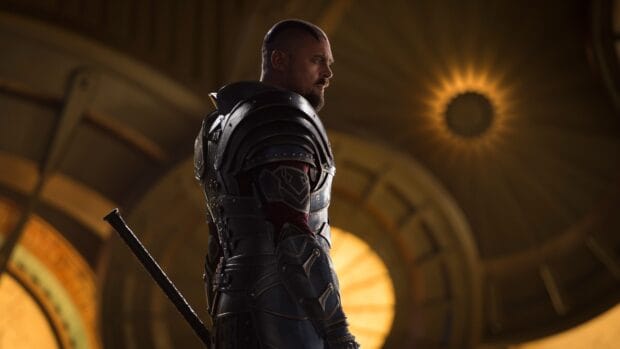 Karl Urban stands in detailed armor inside a building with glowing round windows, 4K Desktop Wallpaper