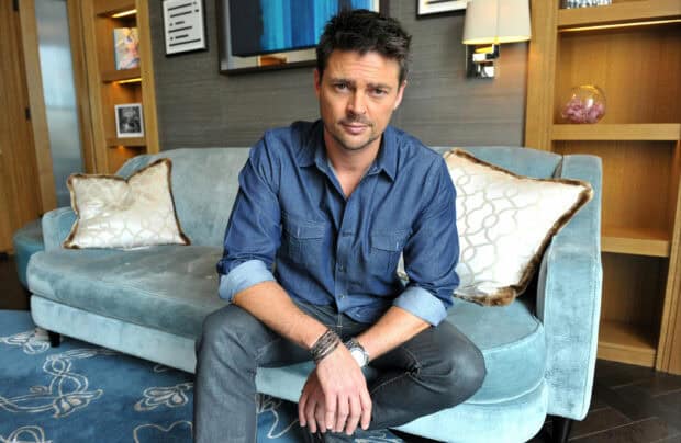 Karl Urban sits casually on a blue couch with a neutral expression, HD Desktop Wallpaper