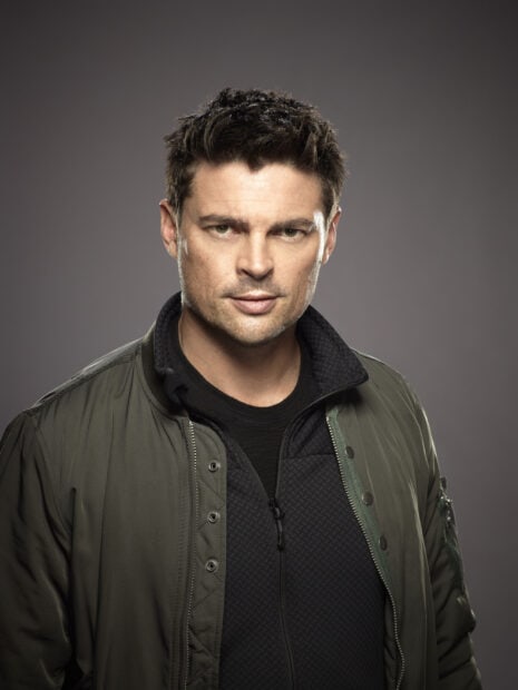 A close up portrait of Karl Urban wearing a green jacket over a black zippered shirt, 2K Mobile Wallpaper