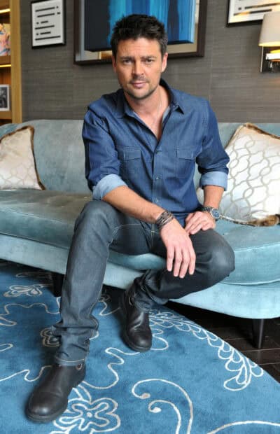 Karl Urban is sitting on a blue couch wearing a denim shirt and black boots, HD Mobile Wallpaper