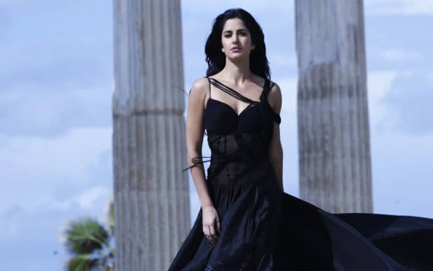 Katrina Kaif Wallpapers shows a woman in a flowing black dress standing confidently outdoors near tall stone pillars, 2K Desktop Wallpaper