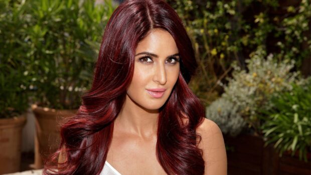 Katrina Kaif with vibrant red hair posing outdoors in a garden setting, 4K Desktop Wallpaper
