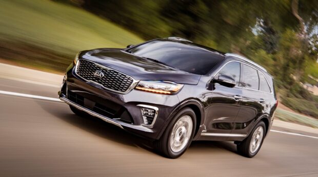 A Kia vehicle is driving swiftly on a suburban road with trees in the background, 2K PC Wallpaper