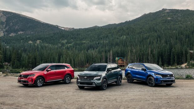 Three Kia SUVs are parked by a lake with forested mountains in the background, HD Desktop Wallpaper