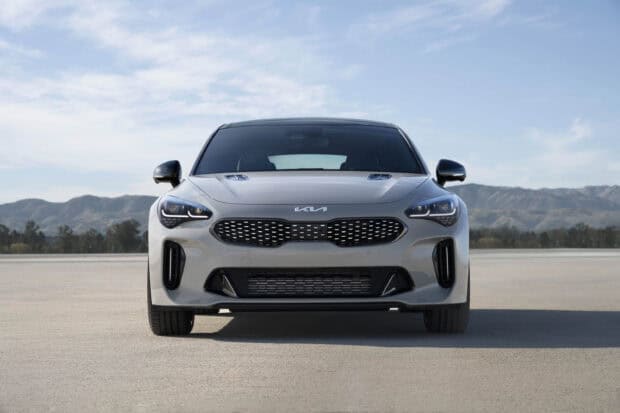 A Kia Stinger is parked on an open road with mountains and a clear sky in the background, 2K Desktop Wallpaper