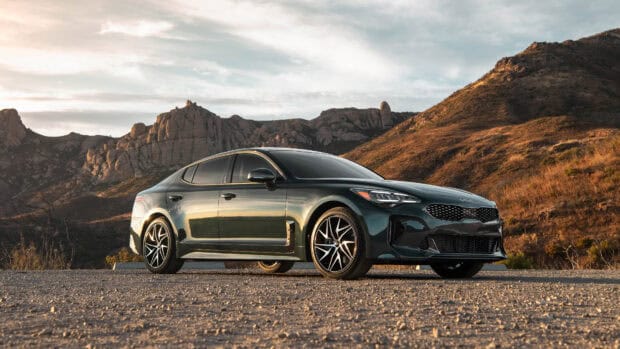 A sleek Kia Stinger is parked on a gravel road with mountains in the background during sunset, 4K Desktop Wallpaper