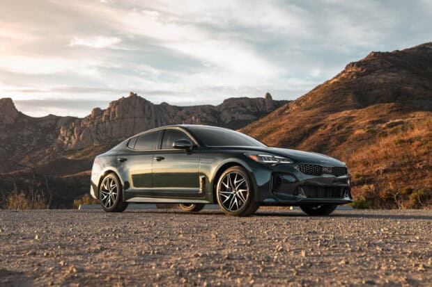 A Kia Stinger is parked on a gravel road with rugged mountains in the background during sunset, 2K Desktop Wallpaper
