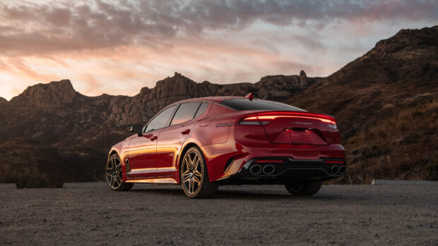 A red Kia Stinger is parked on a dirt road with mountains and a colorful sunset sky in the background, 4K Desktop Wallpaper