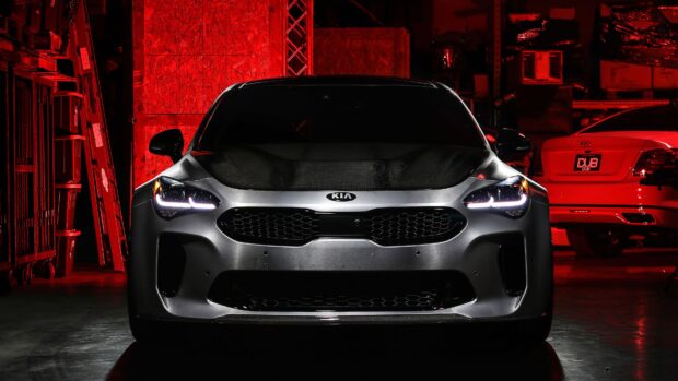 A Kia Stinger is parked indoors with dramatic red lighting highlighting its front grille and headlights, 4K Desktop Wallpaper