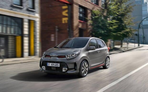 A gray Kia car is driving quickly on a city road surrounded by buildings and trees, HD Desktop Wallpaper