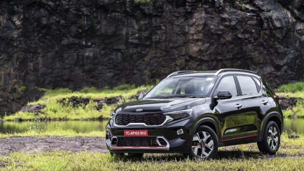 A black Kia car is parked on grass near a rocky cliff in nature, HD Desktop Wallpaper