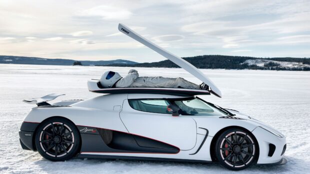 A Koenigsegg is parked on a snowy field with a person lying on its open roof, 4K Desktop Wallpaper