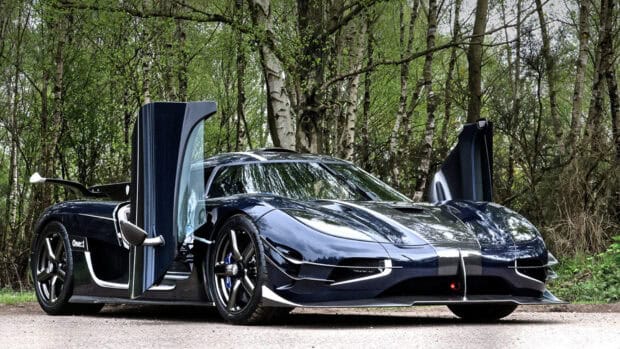 A Koenigsegg One1 with butterfly doors is parked on a road surrounded by trees, HD Desktop Wallpaper