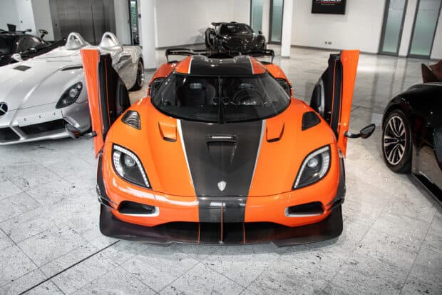 An orange Koenigsegg with its doors open is displayed alongside other luxury cars in a showroom, 2K Desktop Wallpaper