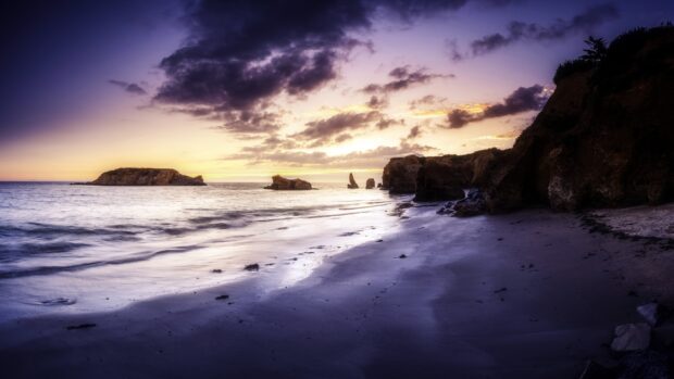 A calm twilight view of Laguna Beach featuring rock formations and gentle waves under a purple sky, 4K Desktop Wallpaper