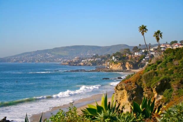 The Laguna Beach Wallpapers show a scenic coastline with waves, cliffs, and houses near the hills, 2K Desktop Wallpaper
