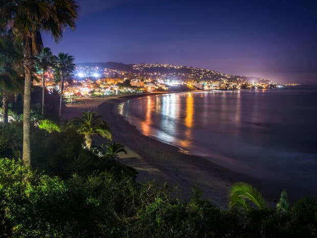 The calm ocean reflects bright lights on the Laguna Beach shore at night, HD Desktop Wallpaper