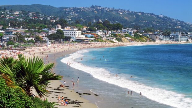 Laguna Beach shows a crowded shore with waves and hills, 2K Desktop Wallpaper