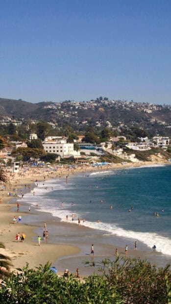 People enjoying the sunny Laguna Beach with hills in the background, 2K Phone Wallpaper