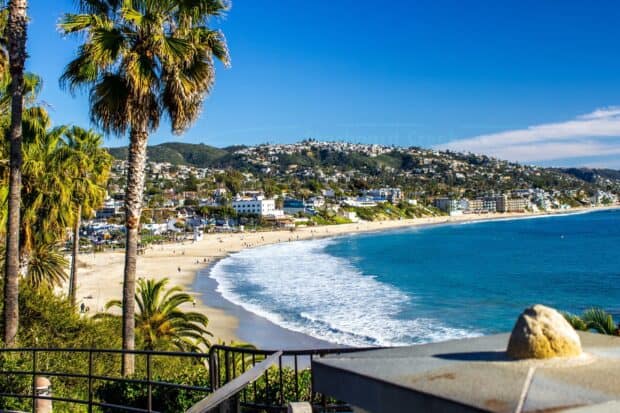 The Laguna Beach coastline stretches with palm trees and waves under a clear blue sky, 2K Desktop Wallpaper