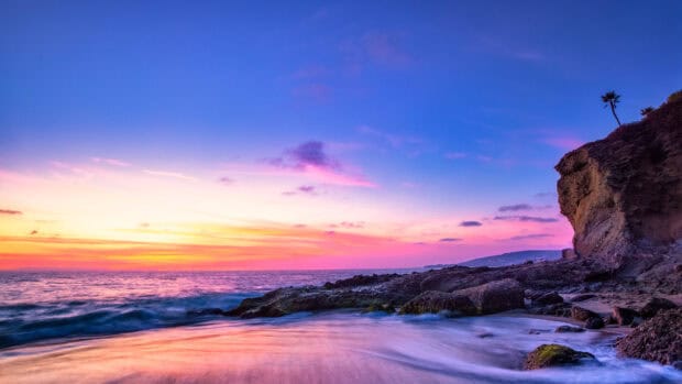 The Laguna Beach wallpapers show a stunning sunset with vibrant colors over rocky shores, 4K Desktop Wallpaper