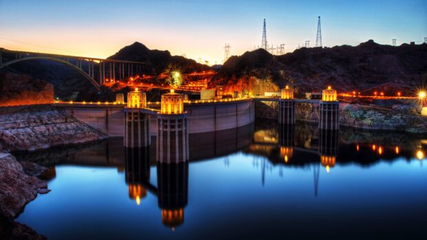 The Lake Mead dam reflects in calm water during sunset with glowing lights, 4K Desktop Wallpaper