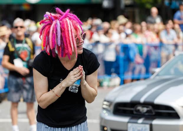 A woman with vibrant pink and purple hair stands smiling at an outdoor event, 2K Desktop Wallpaper