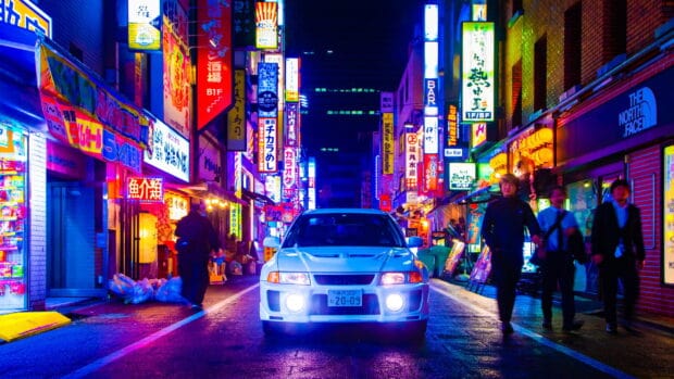 A white Lancer Evo is driving down a vibrant neon lit street with pedestrians around, 2K Desktop Wallpaper