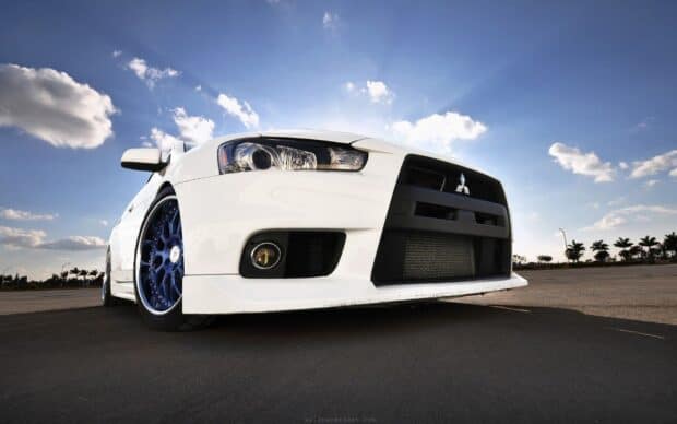 A white Lancer Evo with blue wheels is parked on an open road under a clear sky, HD Desktop Wallpaper
