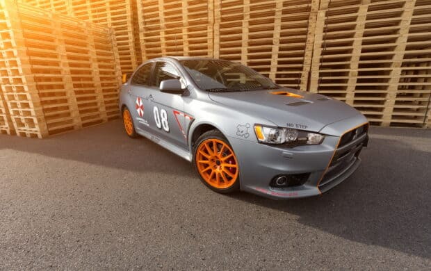 A Lancer Evo with orange wheels parked on asphalt near stacked wooden pallets, 2K Desktop Wallpaper